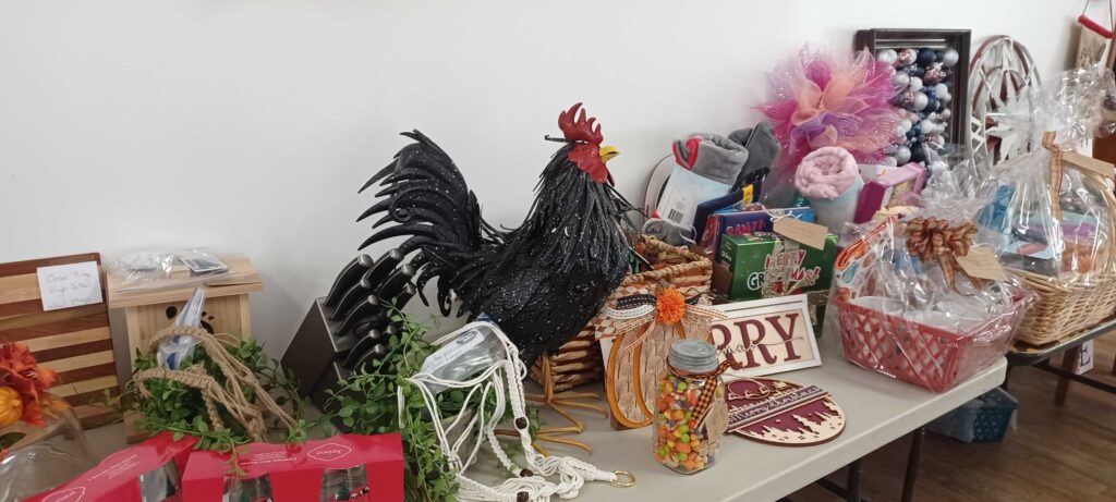 A table with assorted gift baskets, a knife set and a life size metal rooster!